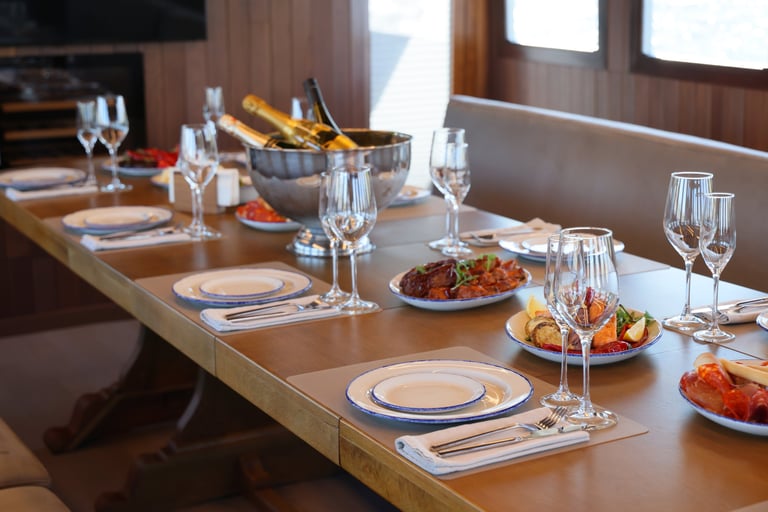 A lavishly decorated dining table awaits, filled with gourmet dishes and chilled champagne in a stunning yacht setting
