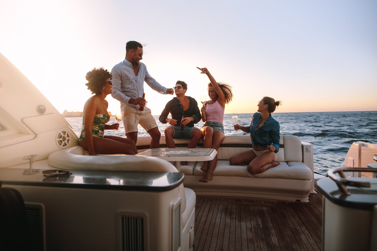 Group of happy friends having a boat party at sunset