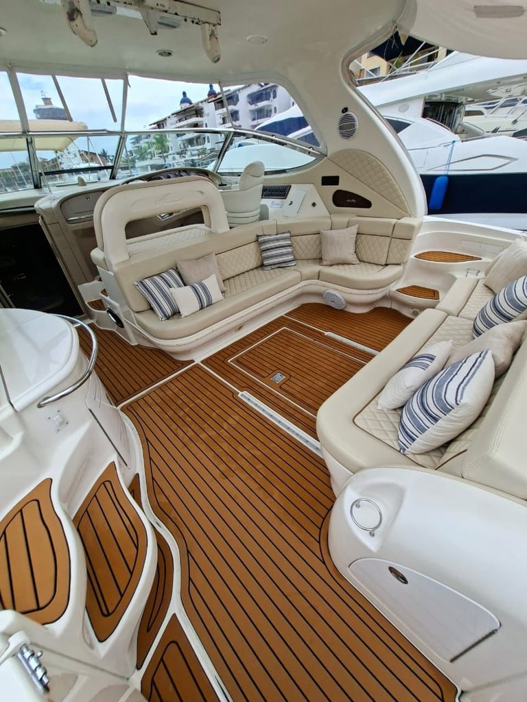 Luxury yacht interior cabin with cream upholstered seating, wooden deck flooring, and large windows overlooking marina