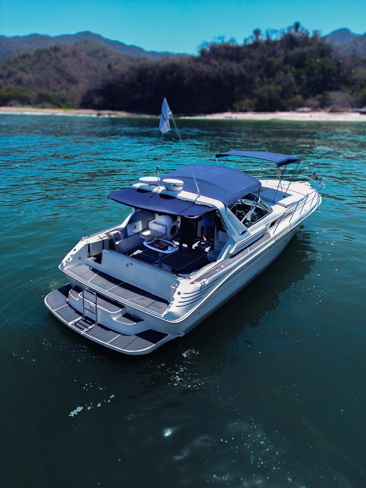 White and blue motorboat with canopy anchored in turquoise water near sandy beach and forested mountains