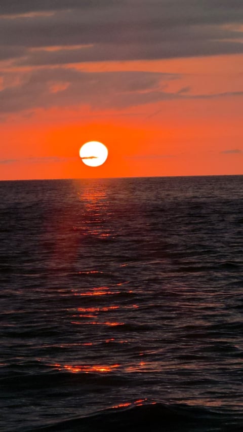 Bright sun setting over ocean with orange sky and golden light reflecting on dark water
