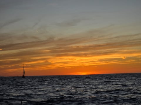 Sailboat on ocean at sunset with golden and orange sky reflecting on water