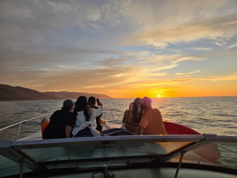 Group of people on a boat watching a golden sunset over the ocean with mountains in the distance