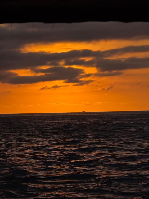 Dramatic orange and gray sunset sky over dark ocean waters with dramatic cloud formations